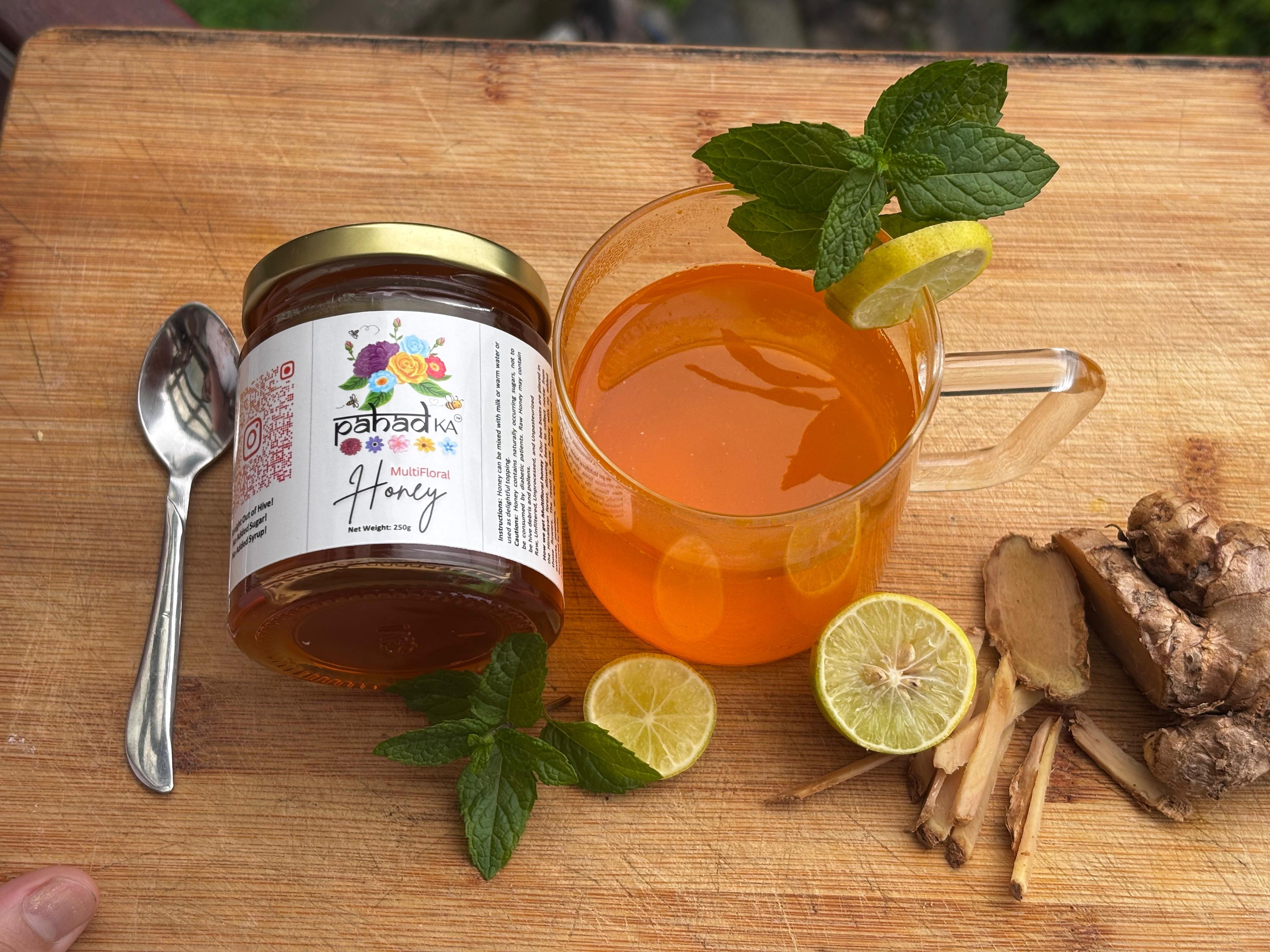 Jar of honey, glass of tea with lemon and mint, and ginger root on a wooden surface.